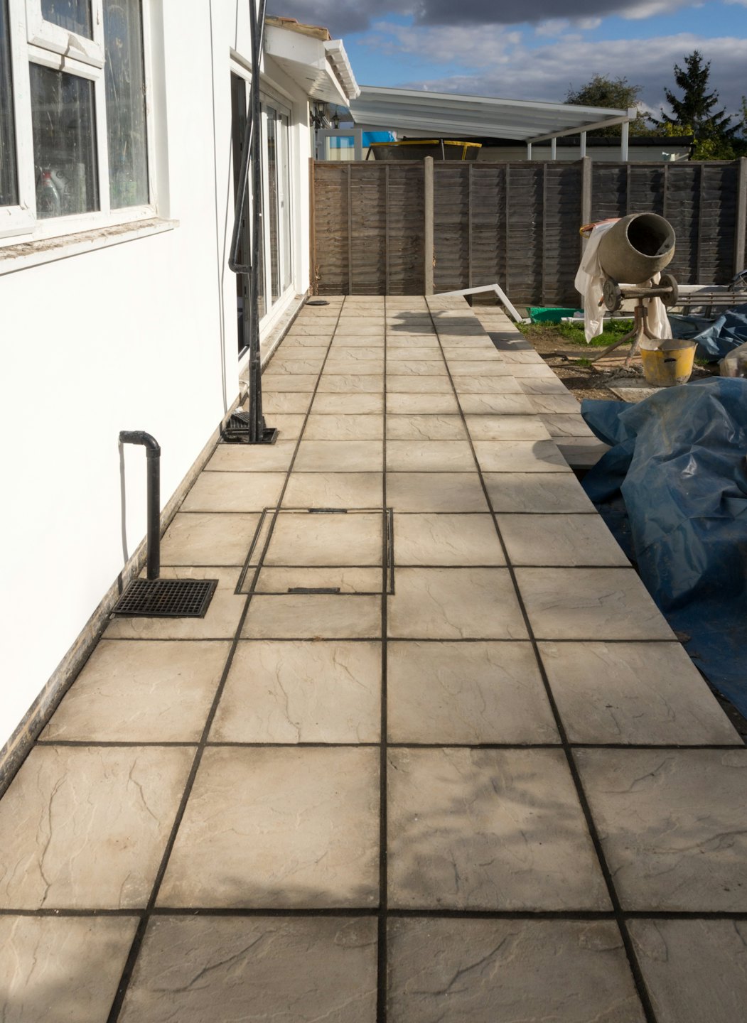 Construction equipment sits on a newly laid patio near a house.